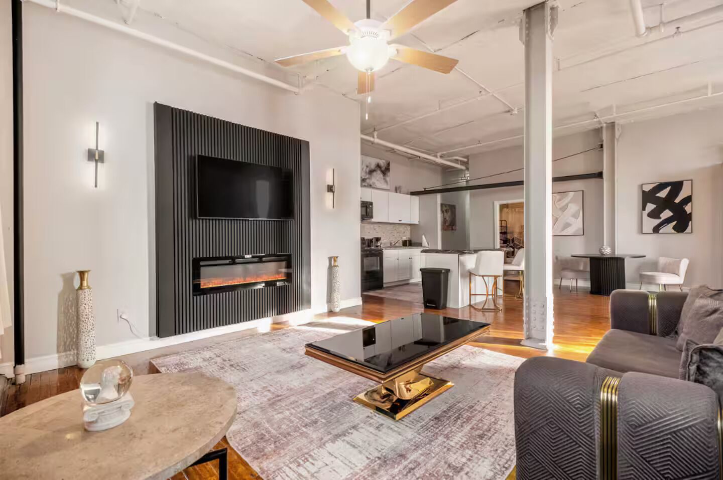 A modern living room with a flat-screen TV, a fireplace, a dining area, and a kitchen in the background.