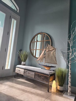 Ein Zimmer mit einem runden Spiegel, einem Modell eines Segelboots, einer Bank mit Schubladen und Blumentöpfen.