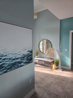 A room with a large wall mural of the ocean, a round mirror, a sailboat model, and a potted plant. - Luxury Waterfront Pool Home Minutes from Boca Grande and Englewood Beaches! (Port Charlotte)