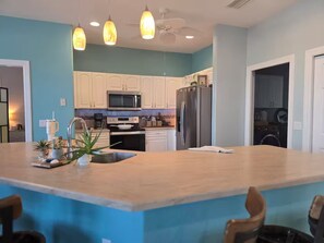 Une cuisine moderne dotée d’un îlot central, de meubles blancs, d’appareils électroménagers en acier inoxydable et de luminaires suspendus.