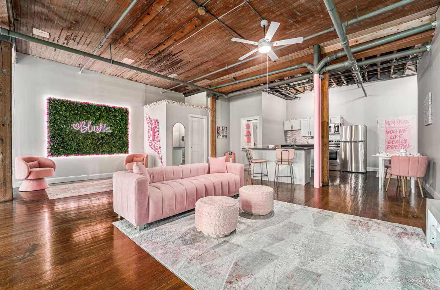 Uma sala de estar moderna com um sofá rosa, pufes e um painel decorativo.