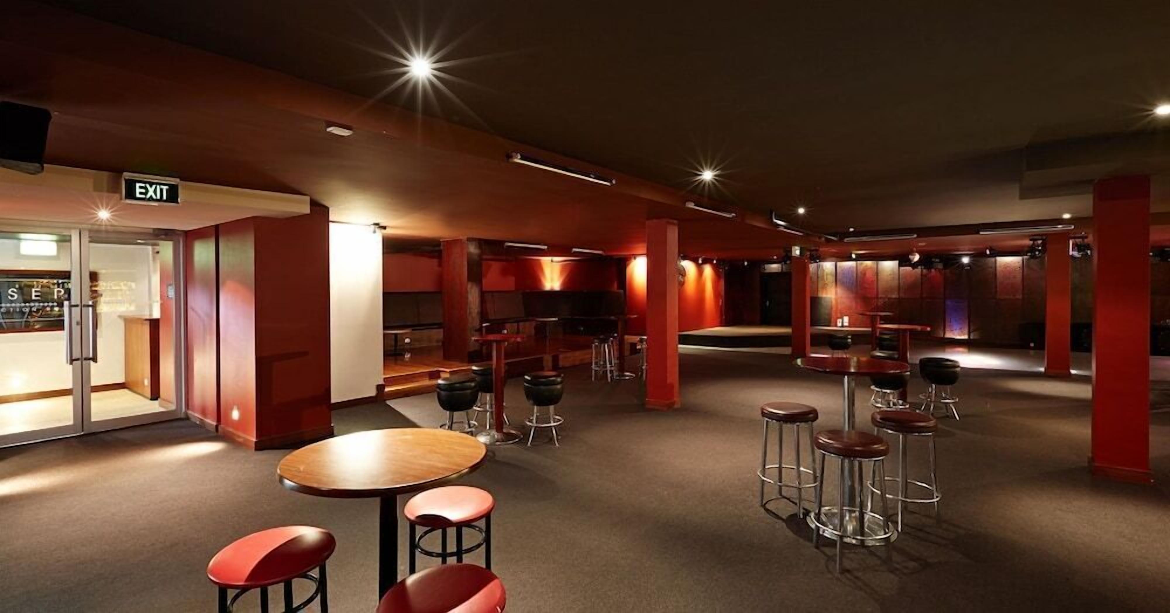 A modern bar area with round tables and stools, an exit sign, and a bar counter.