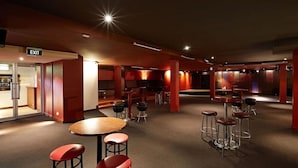 A modern bar area with round tables and stools, an exit sign, and a bar counter. - Waltzing Matilda Hotel (Melbourne)