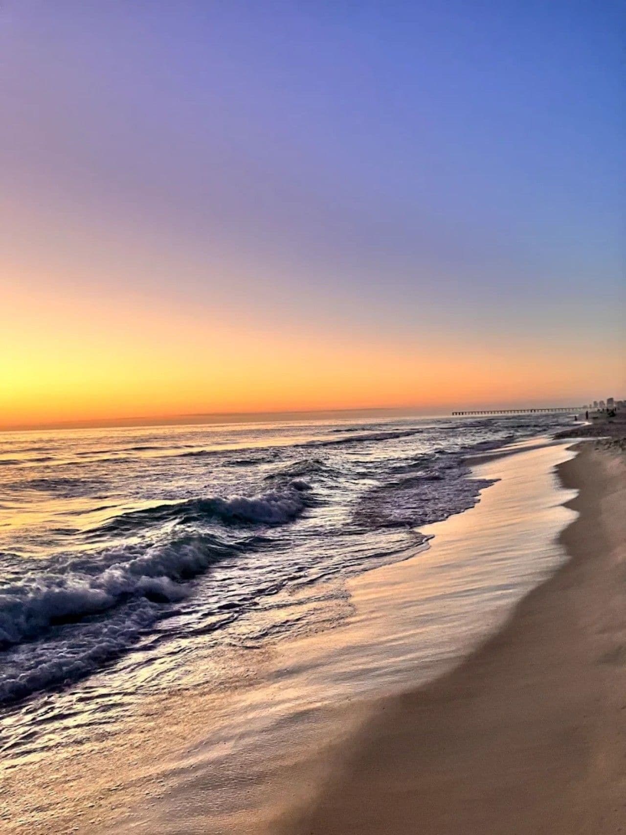 Una playa con olas, un muelle y cielo despejado.