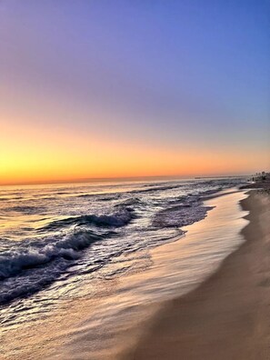 Ein Strand mit Wellen, einem Steg und blauem Himmel.
