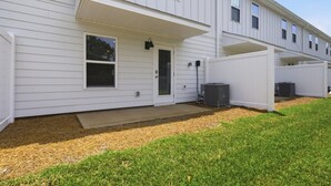 En tvåvånings bostadsbyggnad med en inglasad veranda, en ytterdörr och två luftkonditioneringsaggregat.