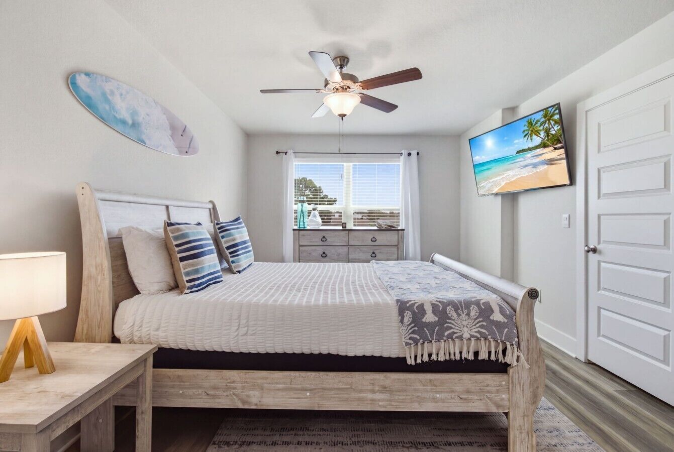A bedroom with a bed, a ceiling fan, a TV, a window with curtains, and a door.