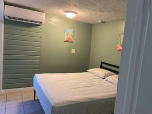 A room with a bed, an air conditioning unit, and two wall-mounted paintings. - Cozy 1BR Apartment Near Downtown Sarasota & Beaches, Pet-Friendly, Sleeps 3 (Sarasota)