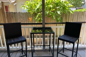 Ein Balkon mit zwei schwarzen Korbstühlen und einem kleinen Tisch, umgeben von einem Holzzaun und Grünpflanzen.
