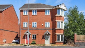 A two-story brick residential building with a red door, white-framed windows, and a small porch. - Cozy 4-Bed Birkenhead Home, Ideal for Contractors (Merseyside)