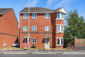A two-story brick residential building with a red door, white-framed windows, and a small porch. - Cozy 4-Bed Birkenhead Home, Ideal for Contractors (Merseyside)