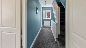A hallway with a carpeted floor, a staircase with white railings, and a ceiling light fixture. - Cozy 4-Bed Birkenhead Home, Ideal for Contractors (Merseyside)