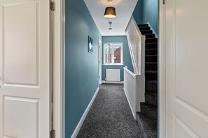 A hallway with a carpeted floor, a staircase with white railings, and a ceiling light fixture. - Cozy 4-Bed Birkenhead Home, Ideal for Contractors (Merseyside)