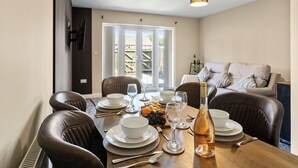 A dining area with a table set for four, chairs, a bottle of wine, and a view of the outside. - Cozy 4-Bed Birkenhead Home, Ideal for Contractors (Merseyside)