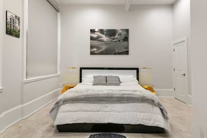 A bedroom with a bed, two bedside lamps, a wall-mounted picture, and a door.