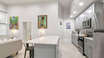 A modern kitchen with stainless steel appliances, a marble countertop, and artwork on the walls.