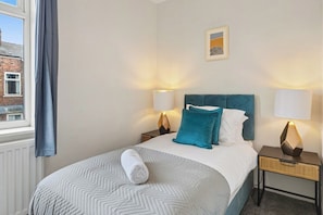 Une chambre d’hôtel comprenant un lit, deux tables de chevet avec des lampes, une fenêtre avec des rideaux et un tableau accroché au mur.