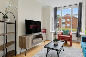 Un salon comprenant un téléviseur, un canapé, une table basse et une fenêtre donnant sur une maison.