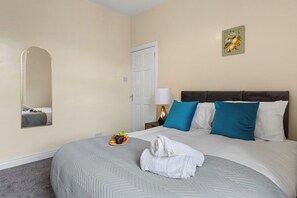 A hotel room with a bed, a bedside table, a lamp, and a wall-mounted mirror. - Stylish 3BR Mellor House close to Old Trafford (Stretford)
