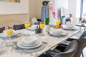A dining table set with plates, glasses, and cutlery, with a vase of flowers and a fruit bowl on the table. - Stylish 3BR Mellor House close to Old Trafford (Stretford)