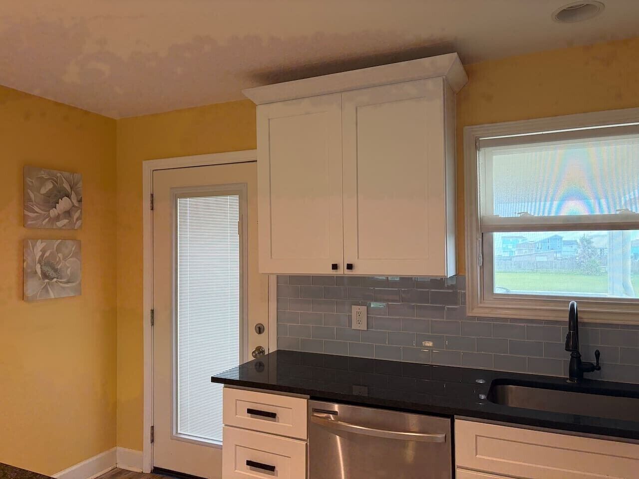 A kitchen with white cabinets, a black countertop, and a window with blinds.