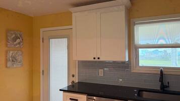 A kitchen with white cabinets, a black countertop, and a window with blinds.