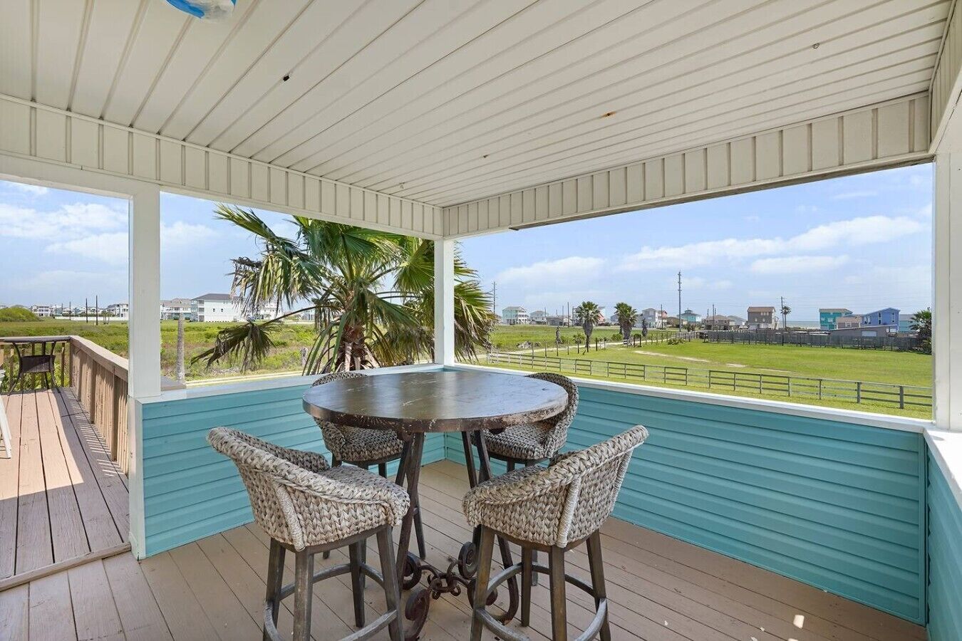 A covered outdoor area with a round table and four chairs, a view of the beach, and a clear sky.