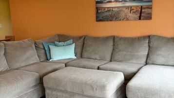 A living room with a sectional sofa, a small ottoman, and a painting on the wall.