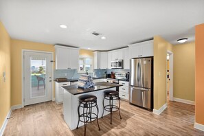 A modern kitchen with white cabinets, a stainless steel refrigerator, and a bar area with stools. - Private Paradise w/Hot Tub @ The SeaBird (Galveston)
