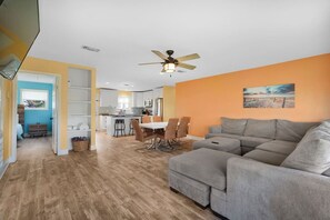 A spacious living room with a gray sectional sofa, a dining area with a table and chairs, and a kitchen in the background. - Private Paradise w/Hot Tub @ The SeaBird (Galveston)