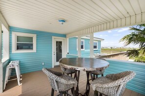 A covered outdoor area with a round table and wicker chairs, a door, and a view of the beach. - Private Paradise w/Hot Tub @ The SeaBird (Galveston)
