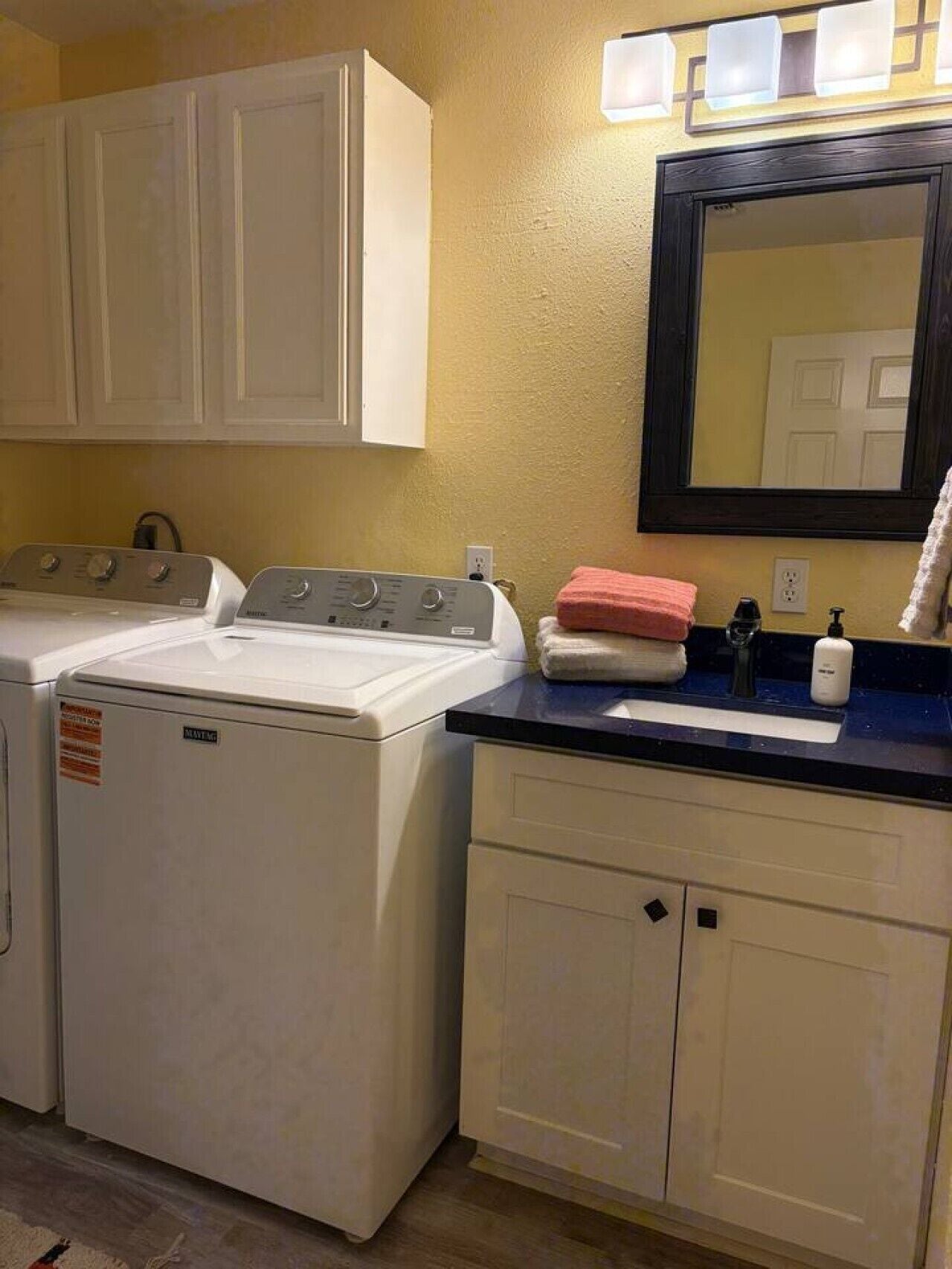 A laundry area with two washing machines, a sink with a mirror above it, and a towel rack.