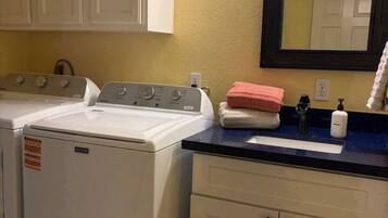 A laundry area with two washing machines, a sink with a mirror above it, and a towel rack.