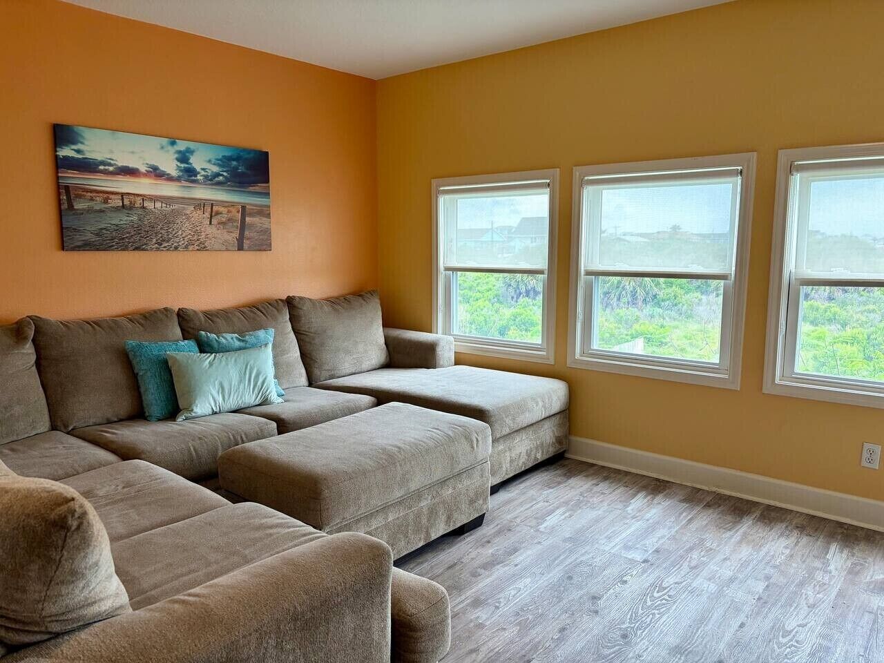 A living room with a sectional sofa, two windows, and a painting on the wall.