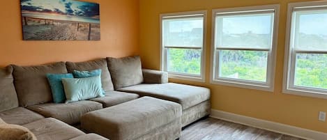 A living room with a sectional sofa, two windows, and a painting on the wall.