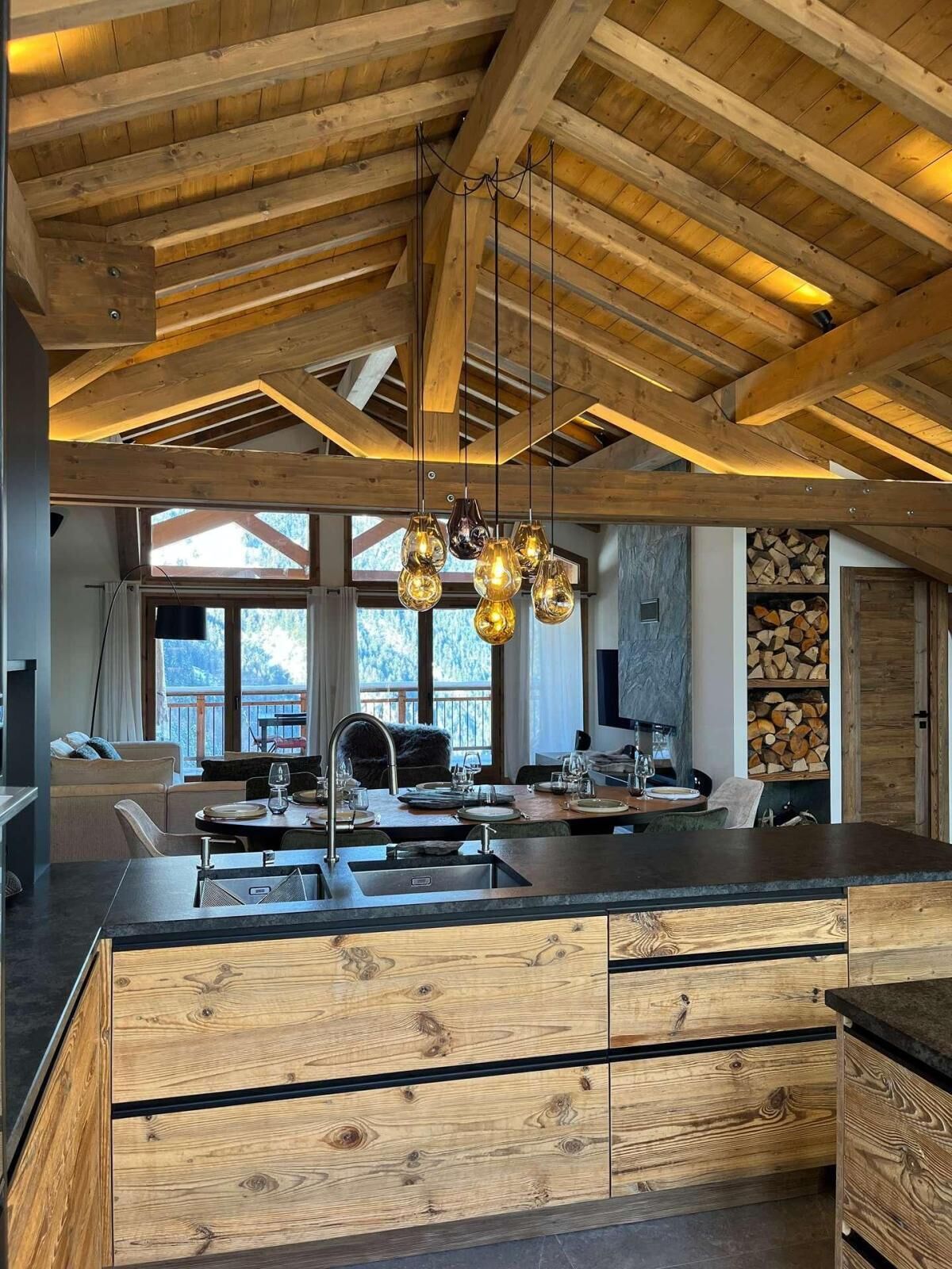 Une cuisine moderne avec un plafond en bois, un îlot central doté d’un évier et un coin repas offrant une vue agréable.
