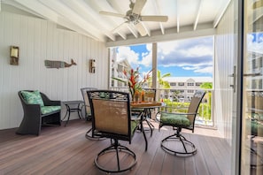 A covered outdoor area with a ceiling fan, a table with chairs, and a view of buildings in the background. - Rum Fun Sun at Lantana No. 25 | Refreshed 1BR, 2 Pools, West Coast Barbados (St. James)