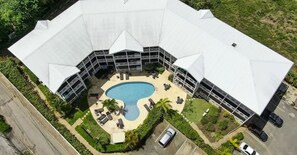 A hotel with a large swimming pool surrounded by lounge chairs and umbrellas, a covered outdoor area, and a parking lot. - Rum Fun Sun at Lantana No. 25 | Refreshed 1BR, 2 Pools, West Coast Barbados (St. James)