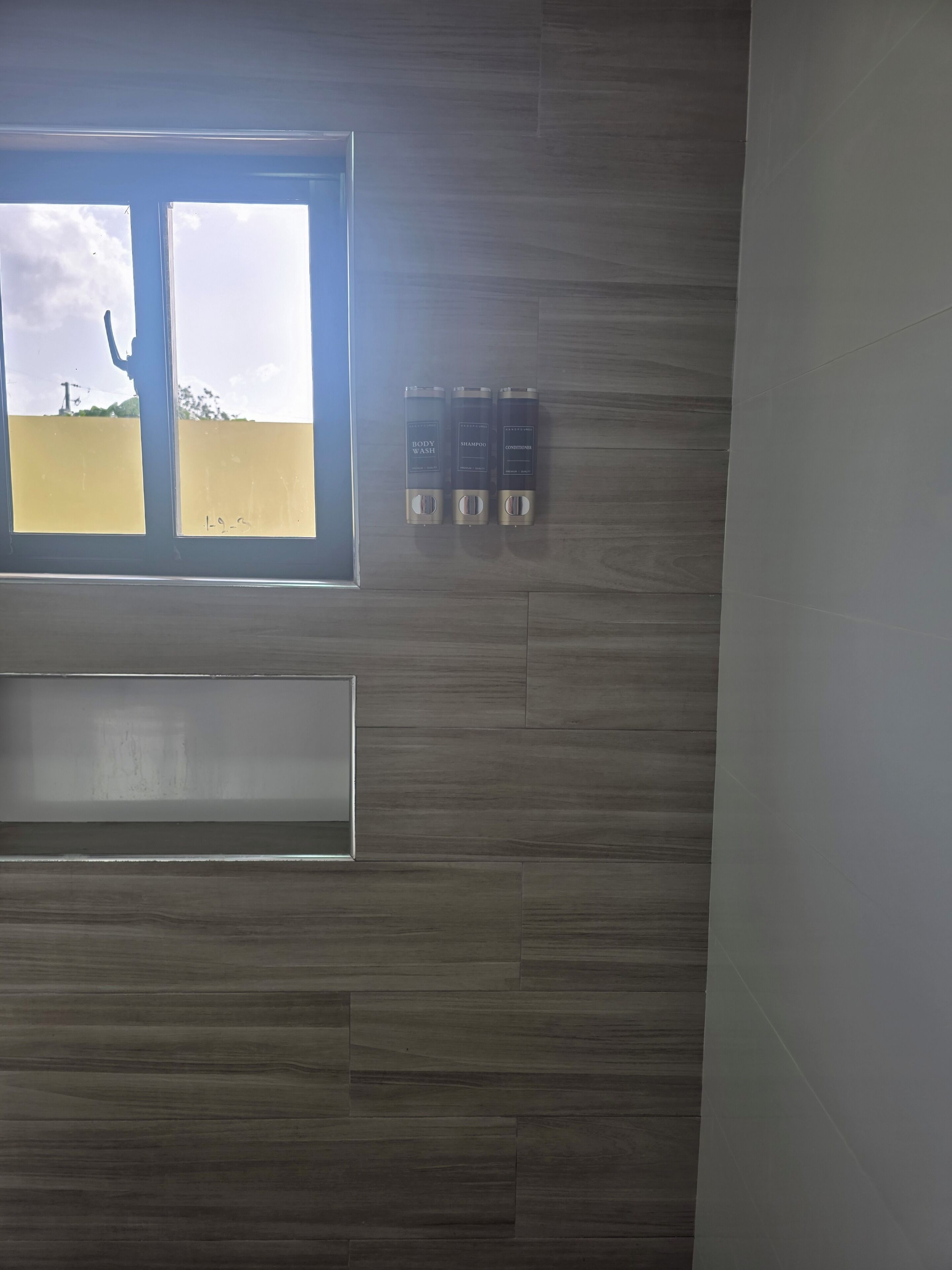 Un baño con pared de madera, una ventana y tres botellas de champú y acondicionador.