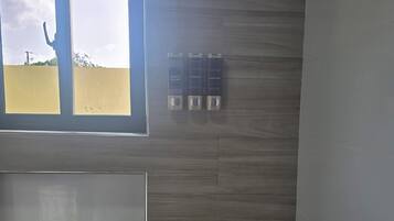 Un baño con pared de madera, una ventana y tres botellas de champú y acondicionador.
