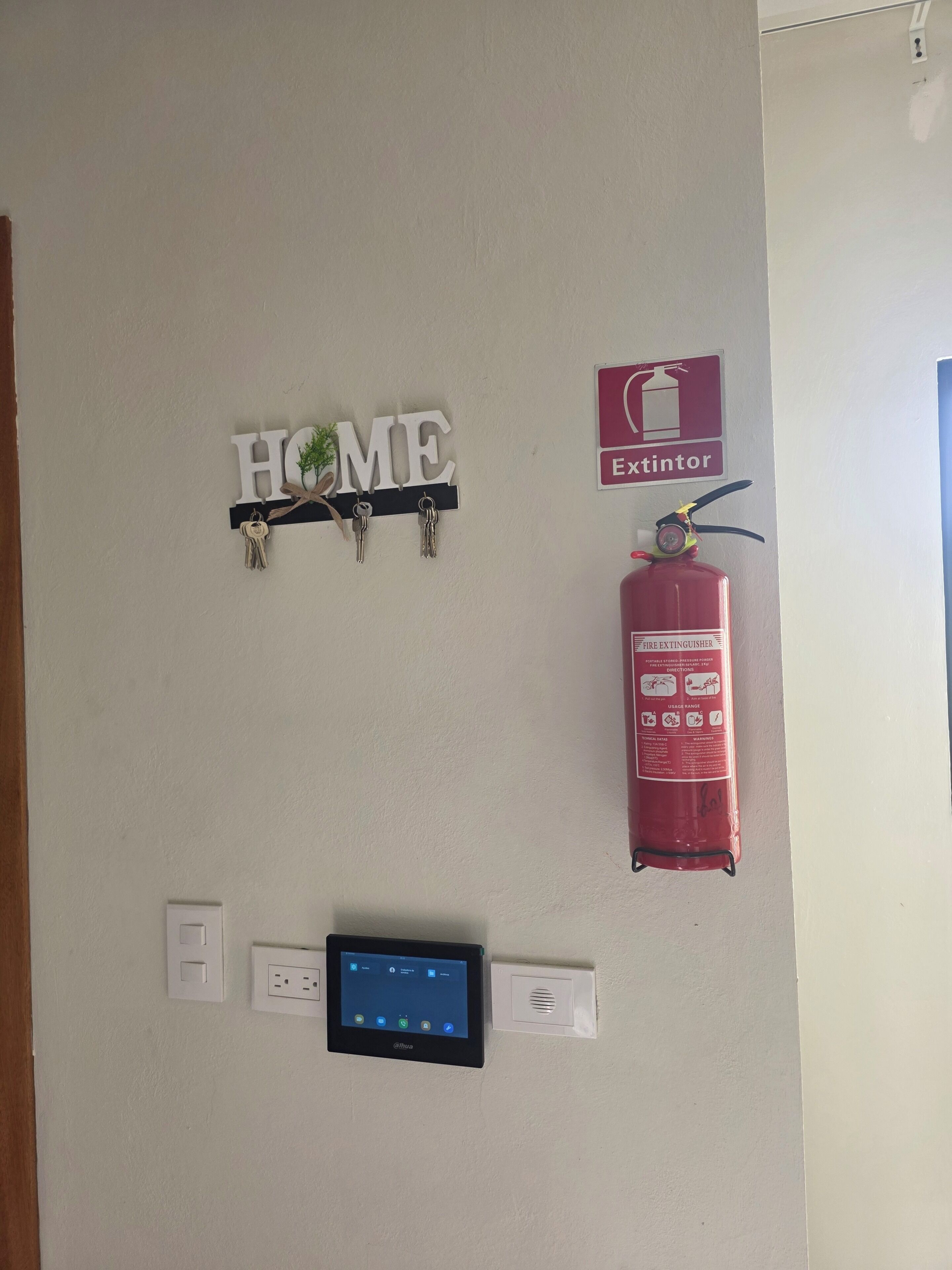 A wall-mounted fire extinguisher, a digital thermostat, and a 'HOME' sign with keys.