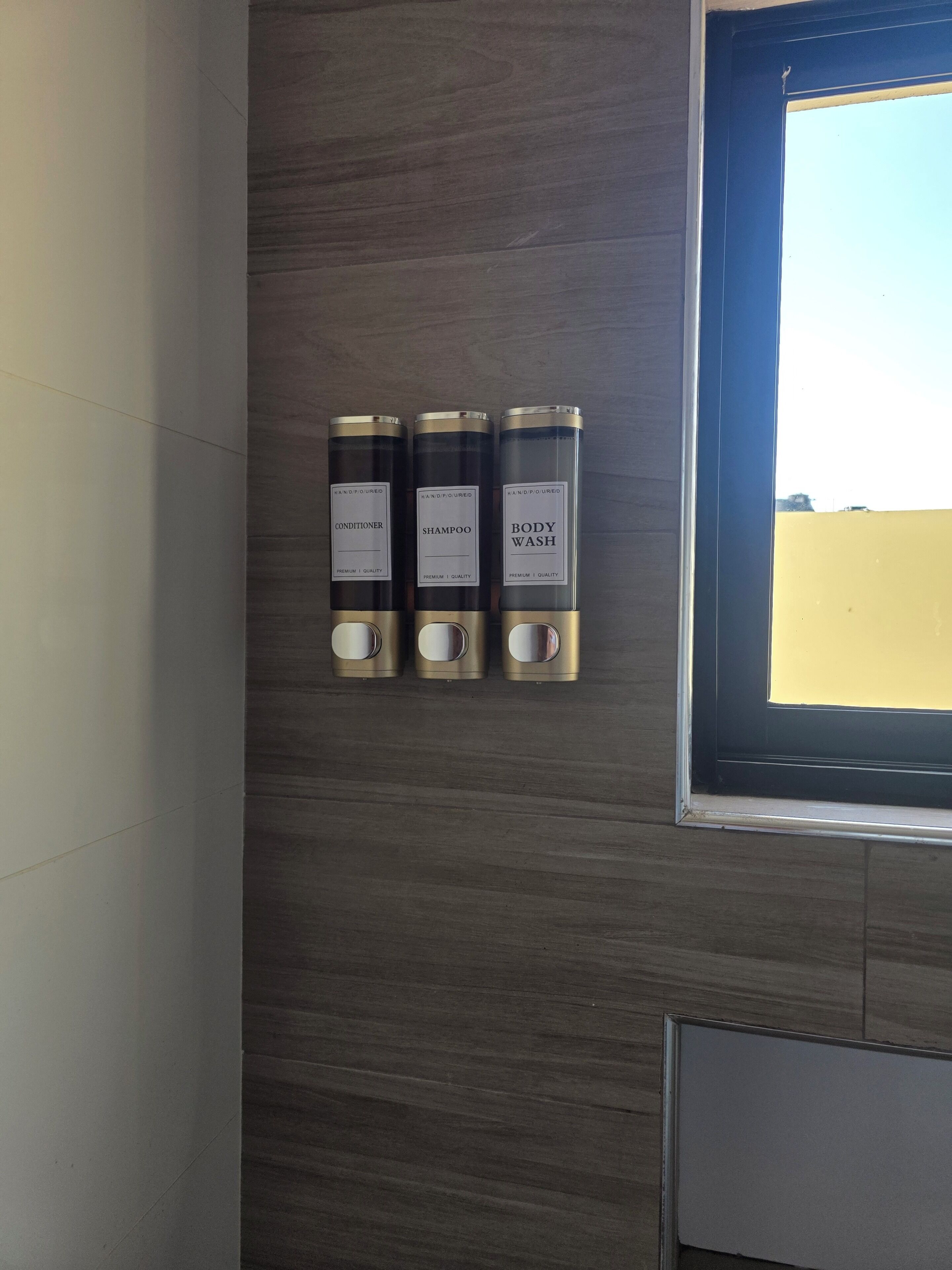 Drei Flaschen handgegossener Conditioner, Shampoo und Duschgel an einer Wand.