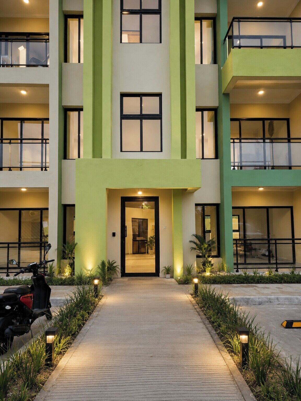 Un edificio moderno con una entrada central, varios balcones y un sendero que conduce a la entrada.