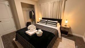 Un lit bien fait, recouvert d’une couverture à carreaux noirs et blancs, un peignoir blanc et une petite table de chevet avec une lampe.