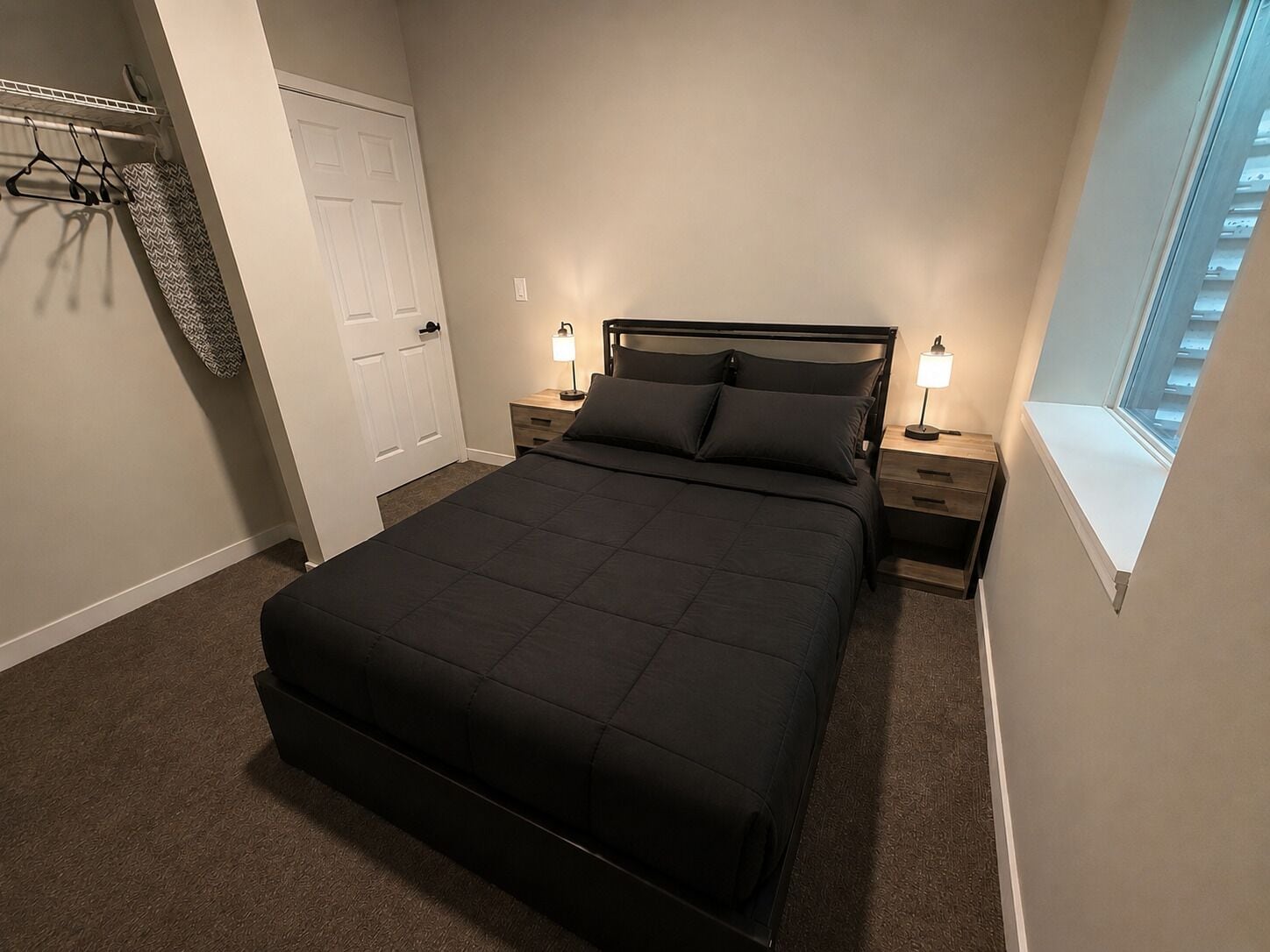 Un dormitorio con una cama grande, dos mesitas de noche con lámparas, un armario con puerta y una ventana con vistas.