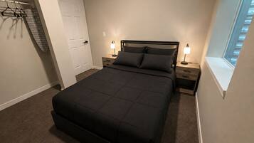 Un dormitorio con una cama grande, dos mesitas de noche con lámparas, un armario con puerta y una ventana con vistas.
