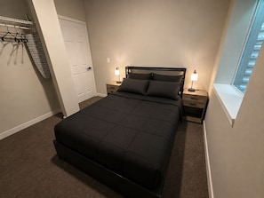 Un dormitorio con una cama grande, dos mesitas de noche con lámparas, un armario con puerta y una ventana con vistas.