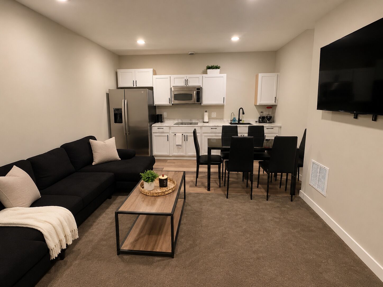 A living room with a black sofa, a coffee table, and a TV mounted on the wall.