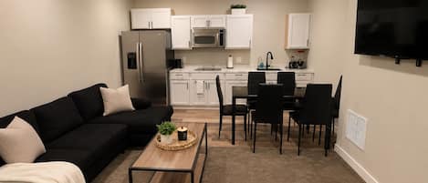 A living room with a black sofa, a coffee table, and a TV mounted on the wall.