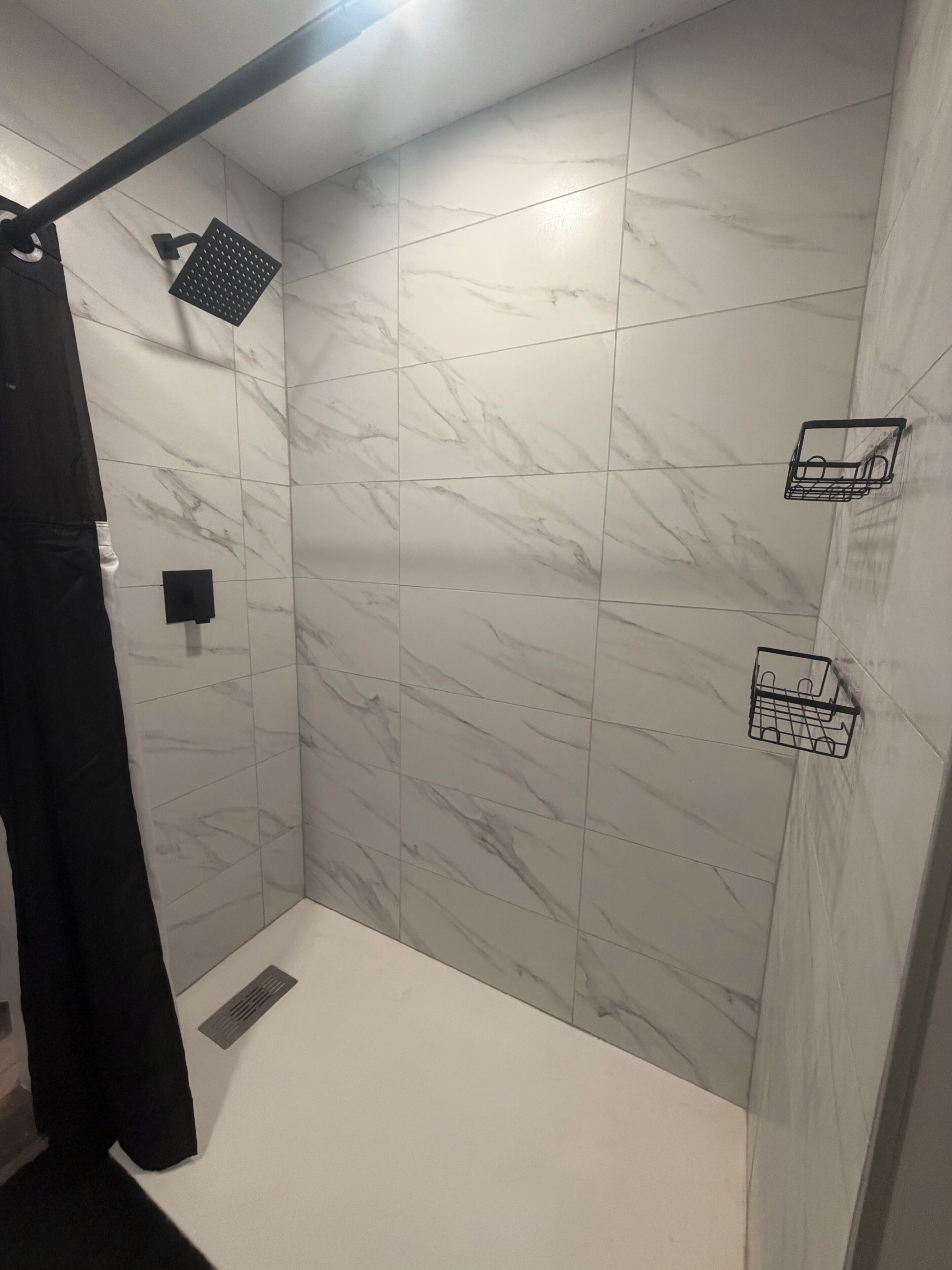 Un espacio de ducha con pared de mármol blanco, una toalla negra y un pequeño estante negro.